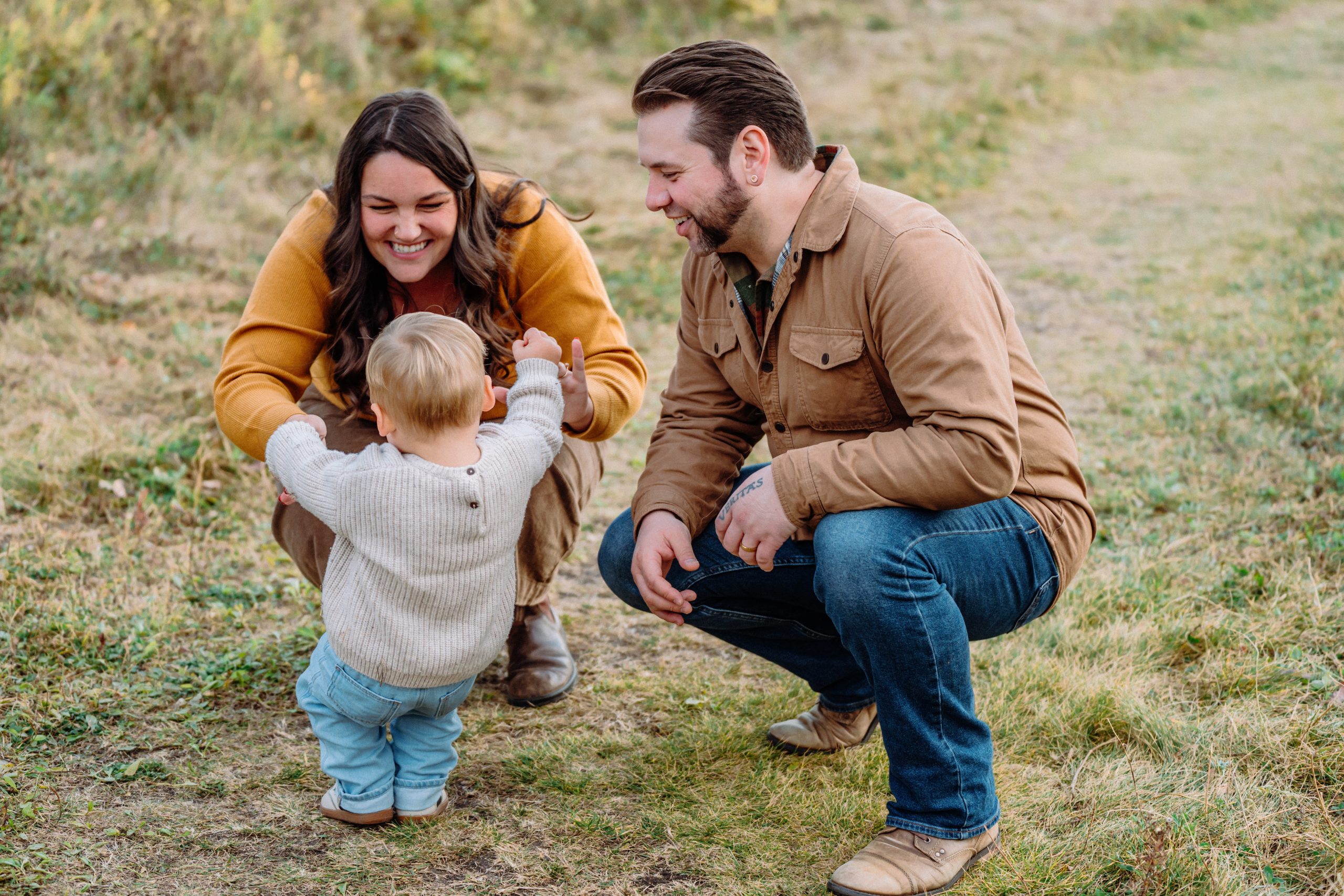 Family Moment Outdoors in Rural Alberta Two adults smiling and kneeling outdoors while a young child takes steps toward them